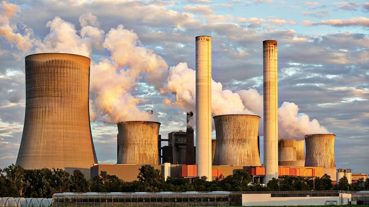 View of a power plant with smoke emissions under a cloudy sky, depicting industrial energy production.